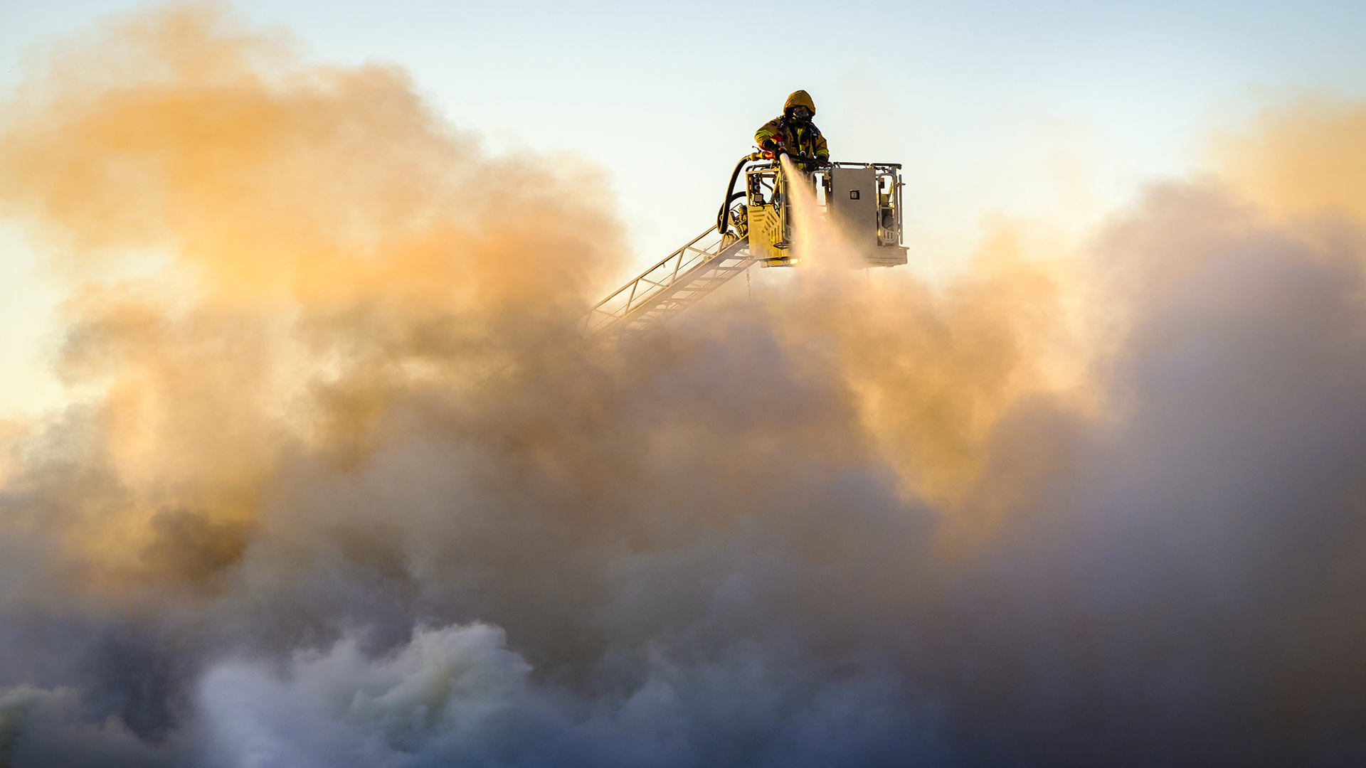 Genrebild på en brandman som står mitt i ett stort rökmoln och sprutar vatten.